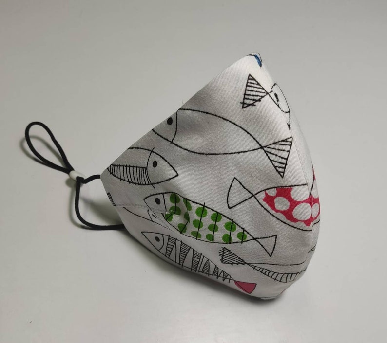 May include: White face mask with a black and white fish pattern. The fish have green and red polka dots.
