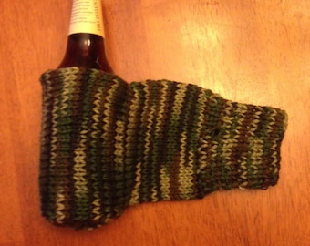 May include: A green, brown, and black knitted sock with a brown glass bottle inside. The bottle has a label that says "Cabin Fever".