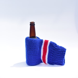 May include: A brown glass bottle with a blue and white knitted bottle cozy with red stripes.
