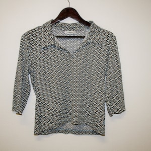 May include: A white, long-sleeved shirt with a geometric pattern in shades of blue and green. The shirt has a collar and a button-up front.