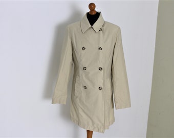 May include: A beige double-breasted trench coat with a classic collar and button details. The coat is displayed on a wooden mannequin against a white background. The coat has long sleeves and a knee-length hem.