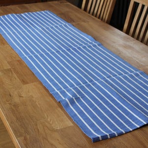 May include: A blue and white striped table runner on a wooden table. The runner has a woven texture and is made of cotton.