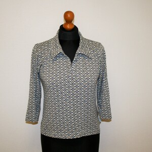May include: A white, blue, and gold patterned long-sleeved shirt with a collar and a zipper closure.