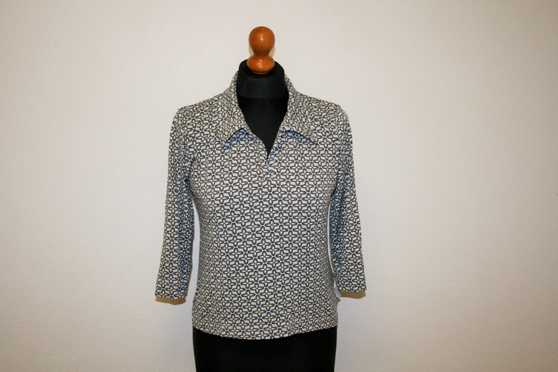May include: A white, blue, and gold patterned long-sleeved shirt with a collar and a zipper closure.