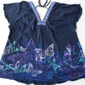 Peut inclure: Un haut bleu marine &agrave; imprim&eacute; papillon. Le haut a un col en V et une cravate au cou. Les papillons sont dans des tons de violet, bleu et vert.