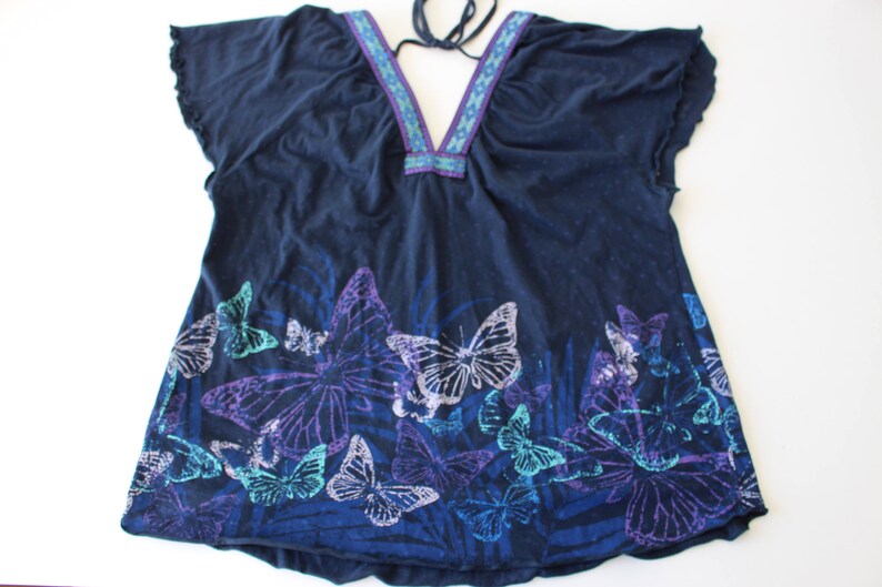 Peut inclure: Un haut bleu marine &agrave; imprim&eacute; papillon. Le haut a un col en V et une cravate au cou. Les papillons sont dans des tons de violet, bleu et vert.