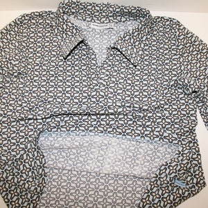 May include: A long-sleeved blue shirt with a white and brown geometric pattern. The shirt has a collar and a button-up front.