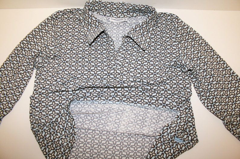 May include: A long-sleeved blue shirt with a white and brown geometric pattern. The shirt has a collar and a button-up front.