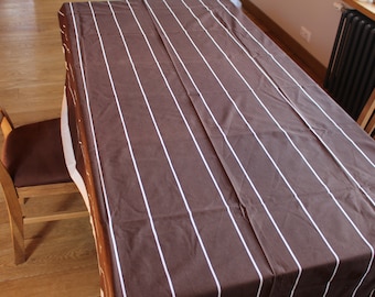 May include: A brown tablecloth with vertical white stripes covers a wooden table. The table is set with two wooden chairs, one on each side. The tablecloth is rectangular and has a simple, classic design.
