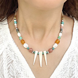 May include: A multi-colored beaded necklace with a white shell pendant. The necklace features beads in shades of orange, pink, green, and white.
