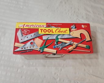 May include: A red metal "American Tool Chest" with various toy tools illustrated on the front. The chest features a yellow banner with the words "TOOL Chest" and "Guaranteed". The tools include a hammer, saw, and pliers.