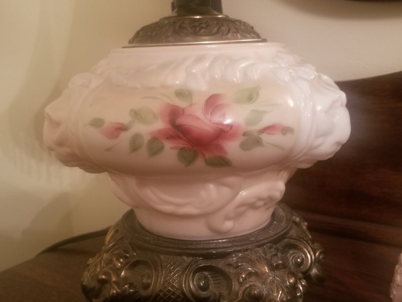 K&ouml;nnte beinhalten: Vintage Tischlampe mit wei&szlig;em Glasschirm mit handgemaltem rosa Rosendesign mit gr&uuml;nen Bl&auml;ttern. Die Lampe hat einen dekorativen, verzierten Metallsockel und einen silberfarbenen Aufsatz.