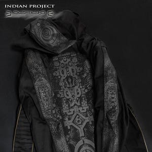 Puede incluir: Chaqueta negra con capucha y complejos patrones geométricos grises en la espalda, mangas y capucha. Cuenta con una cremallera completa y detalles dorados. Se puede ver el texto "INDIAN PROJECT" y "JACKETS FRAKTAL TOTEMIK".
