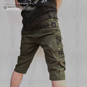 May include: Green cargo shorts with black patterned details and zipper accents. The shorts have a large cargo pocket on the right leg and a smaller pocket on the left leg. The shorts are labeled "Quarter Pants" and "THETA".