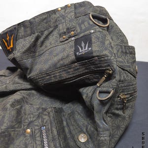 May include: Olive green cargo shorts featuring a repeating geometric star pattern, multiple zippered pockets, brass-toned hardware, and D-ring attachments. A black fabric label displays the text INDIAN PROJECT with a trident logo.