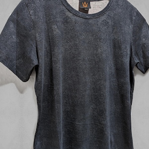 Puede incluir: Una camiseta gris oscura con un patr&oacute;n geom&eacute;trico blanco. La camiseta tiene cuello redondo y mangas cortas. El texto "SHIRTS PLASTIK" es visible en la parte inferior de la imagen.