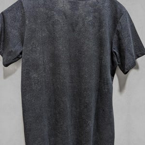 Puede incluir: Una camiseta gris oscura con un patr&oacute;n geom&eacute;trico. La camiseta tiene cuello redondo y mangas cortas. El texto "INDIAN PROJECT" est&aacute; impreso en la parte superior de la camiseta. El texto "SHIRTS PLASTIK" est&aacute; impreso en la parte inferior de la camiseta.