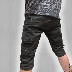 May include: Dark gray cargo shorts featuring a subtle geometric pattern, multiple zippered pockets, and a small black patch with a trident logo on the back waistband. The shorts are paired with a matching gray patterned t-shirt.