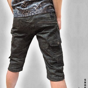 May include: Dark olive green cargo shorts featuring a repeating geometric pattern, multiple utility pockets with zippers and snap buttons, and a metal D-ring. The shorts include a small black label on the back waistband and text reading THETA V2.