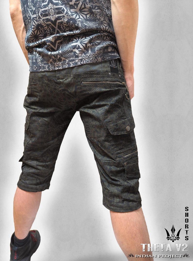May include: Dark olive green cargo shorts featuring a repeating geometric pattern, multiple utility pockets with zippers and snap buttons, and a metal D-ring. The shorts include a small black label on the back waistband and text reading THETA V2.