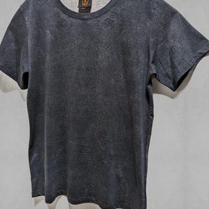 Puede incluir: Una camiseta gris oscura con un patr&oacute;n sutil. La camiseta tiene cuello redondo y mangas cortas. El nombre de la marca "INDIAN PROJECT" est&aacute; impreso en la parte superior de la camiseta.