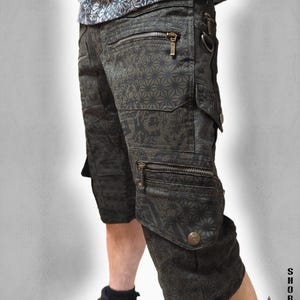Könnte beinhalten: Dunkelgraue Cargoshorts mit einem sich wiederholenden geometrischen Sternenmuster, mehreren Reißverschlusstaschen und seitlichen Cargotaschen mit metallischen Druckknöpfen. Die Shorts verfügen über einen D-Ring und ein passendes Oberteil.