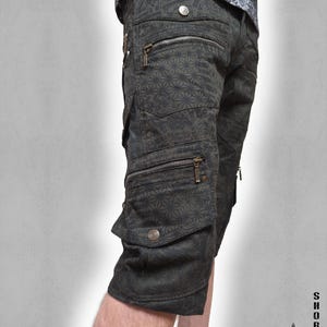 May include: Dark olive green cargo shorts featuring a repeating geometric star pattern. The shorts include multiple pockets with metallic zippers and snap button closures. The text "SHORTS THETA V2 INDIAN PROJECT" is printed in the bottom right corner.