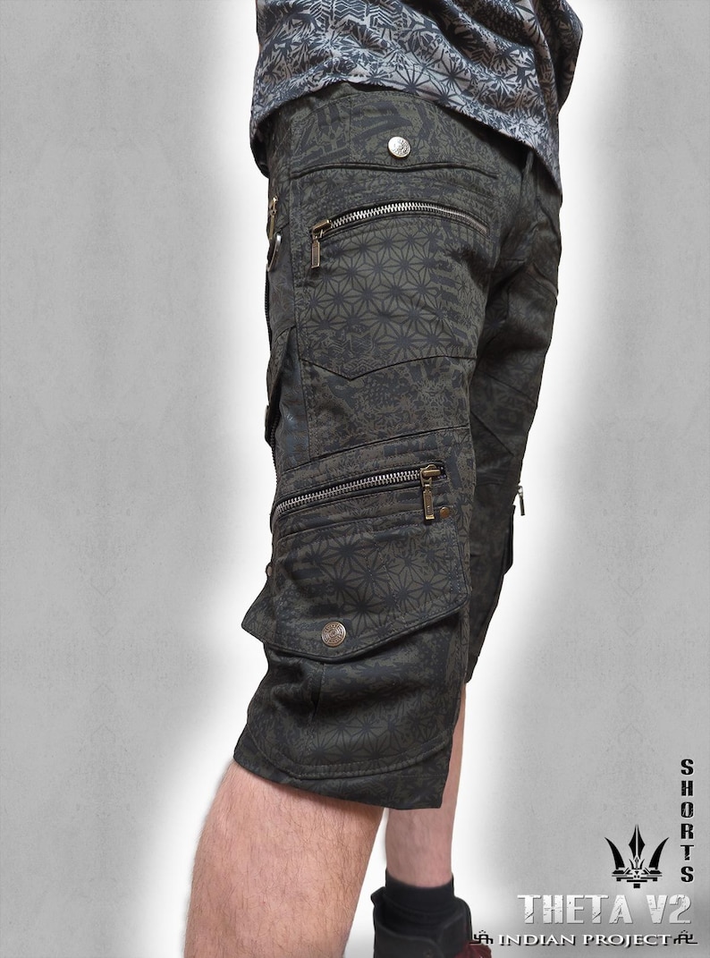 May include: Dark olive green cargo shorts featuring a repeating geometric star pattern. The shorts include multiple pockets with metallic zippers and snap button closures. The text "SHORTS THETA V2 INDIAN PROJECT" is printed in the bottom right corner.