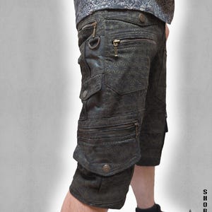 May include: Dark charcoal cargo shorts featuring a repeating geometric star pattern, multiple zippered pockets, metal D-ring hardware, and snap-button closures. The shorts include a side pocket design and are paired with a matching patterned shirt.