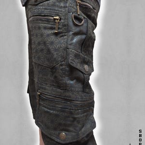 May include: Dark olive green cargo shorts featuring a geometric pattern, multiple zippered pockets, metal D-rings, and snap-button closures. The shorts display the text "SHORTS THETA V2 INDIAN PROJECT" in the lower right corner of the image.