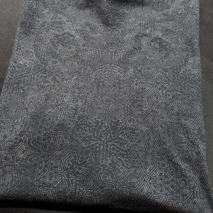 Puede incluir: Una camiseta negra con un patr&oacute;n geom&eacute;trico blanco. La camiseta est&aacute; doblada y sobre una superficie oscura. El texto "SHIRTS PLASTIK" es visible en la esquina inferior derecha de la imagen.