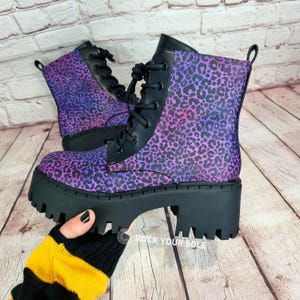 May include: Purple and pink leopard print platform boots with black laces. The boots have a chunky platform sole and a round toe.