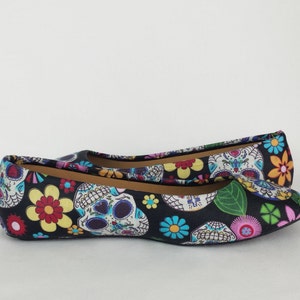 May include: A pair of black ballet flats with a colorful print of sugar skulls and flowers.