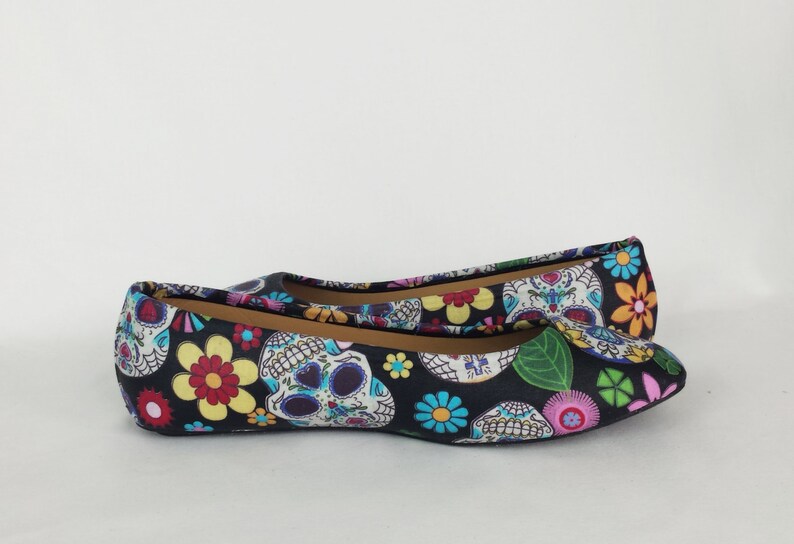 May include: A pair of black ballet flats with a colorful print of sugar skulls and flowers.
