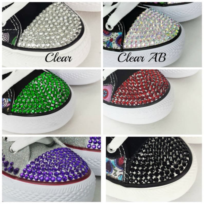May include: Close-up of six different bedazzled sneakers. Each sneaker has a white rubber sole and white laces. The toe caps are covered in clear, clear AB, green, red, purple, and black rhinestones. The text "Clear" and "Clear AB" are visible.