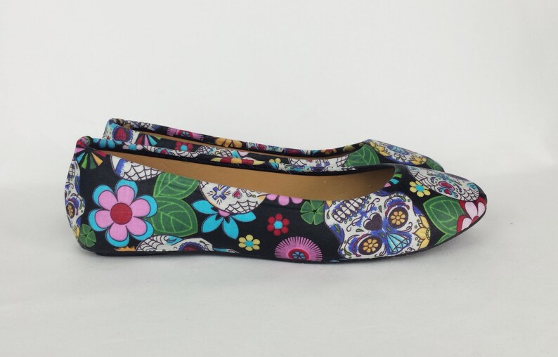 May include: Black ballet flats with a colorful Day of the Dead print featuring skulls, flowers, and leaves.