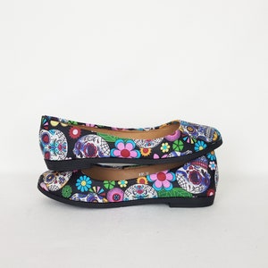 May include: A pair of black ballet flats with a colorful Day of the Dead print featuring sugar skulls and flowers.