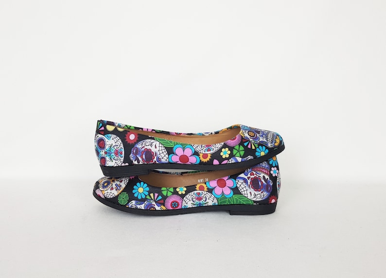 May include: A pair of black ballet flats with a colorful Day of the Dead print featuring sugar skulls and flowers.