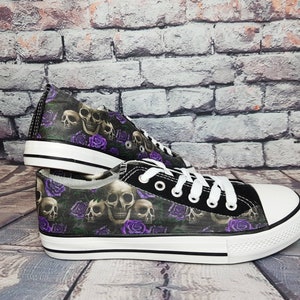 May include: A pair of low-top canvas sneakers featuring a repeating pattern of human skulls and vibrant purple roses on a dark background. The shoes have white rubber toe caps, white laces, and a white rubber sole with a thin black horizontal stripe.