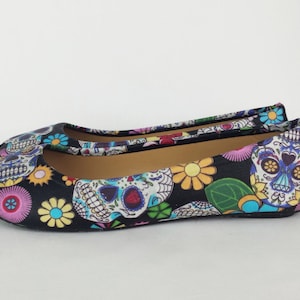 May include: Black ballet flats with a colorful Day of the Dead sugar skull and floral print.
