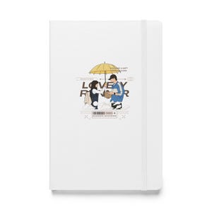 May include: A white notebook featuring a graphic of a couple standing under a yellow umbrella. The text "LOVELY RAINER" is printed in black and the text "YOU ARE A GIFT FROM HEAVEN" is printed in grey. The text "SUDDEN SHOWER" is printed in brown.