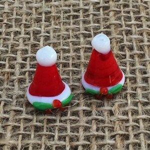 May include: Two small glass Christmas ornaments shaped like Santa hats. The ornaments are red with white trim and green holly accents.