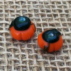 May include: Two small orange and black glass pumpkin beads. The beads have a black center with a small silver dot in the center.