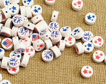 May include: A collection of round white polymer clay beads featuring patriotic designs including red and blue stars, American flag patterns, and blue firework motifs. Each bead has a central hole for stringing, with a smooth, matte finish.