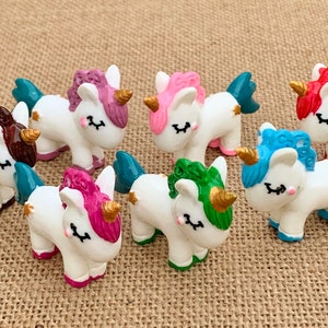 May include: Set of seven small white unicorn figurines with different coloured manes and tails. The unicorns have gold horns and hooves.