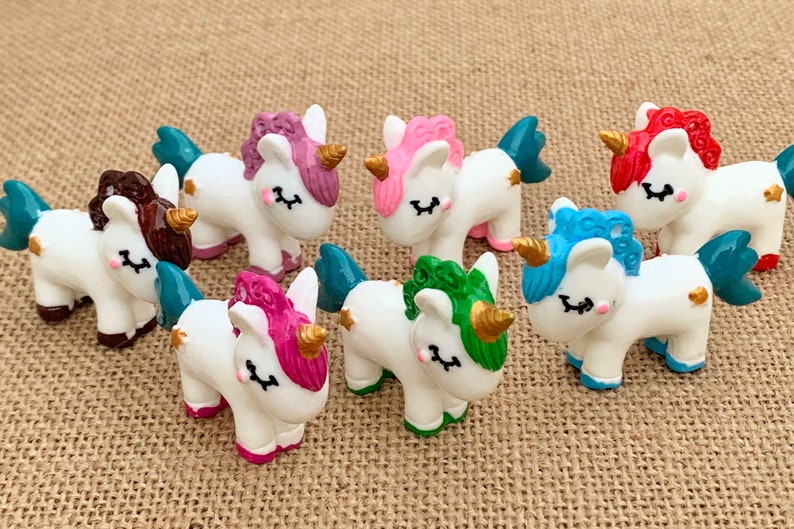May include: Set of seven small white unicorn figurines with different coloured manes and tails. The unicorns have gold horns and hooves.