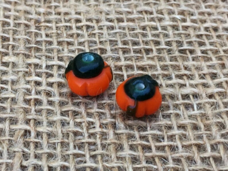 May include: Two small orange and black glass pumpkin beads. The beads have a black center with a small silver dot in the center.