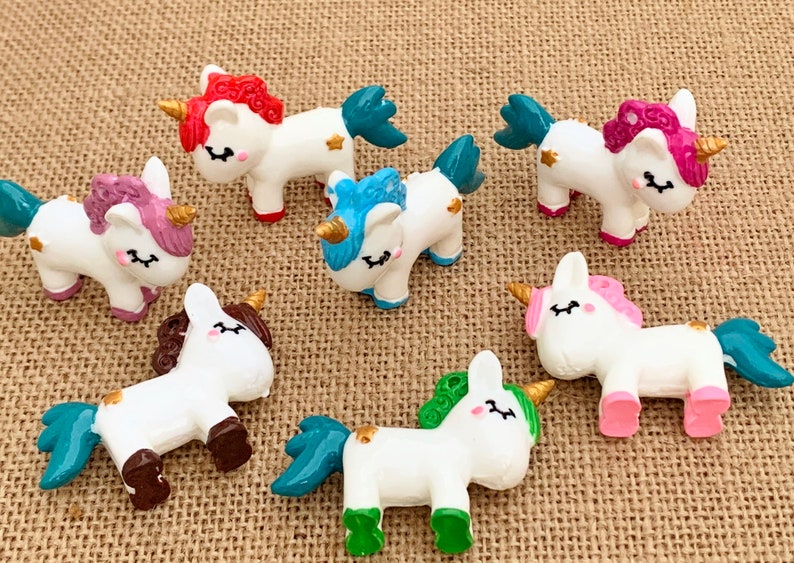 May include: Set of ten small white unicorn figurines with colourful accents. Each unicorn has a different coloured mane and tail, including pink, blue, green, and purple. The unicorns have gold horns and hooves.
