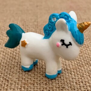 May include: A small white unicorn figurine with a blue mane and tail. The unicorn has a gold horn and a star on its side.