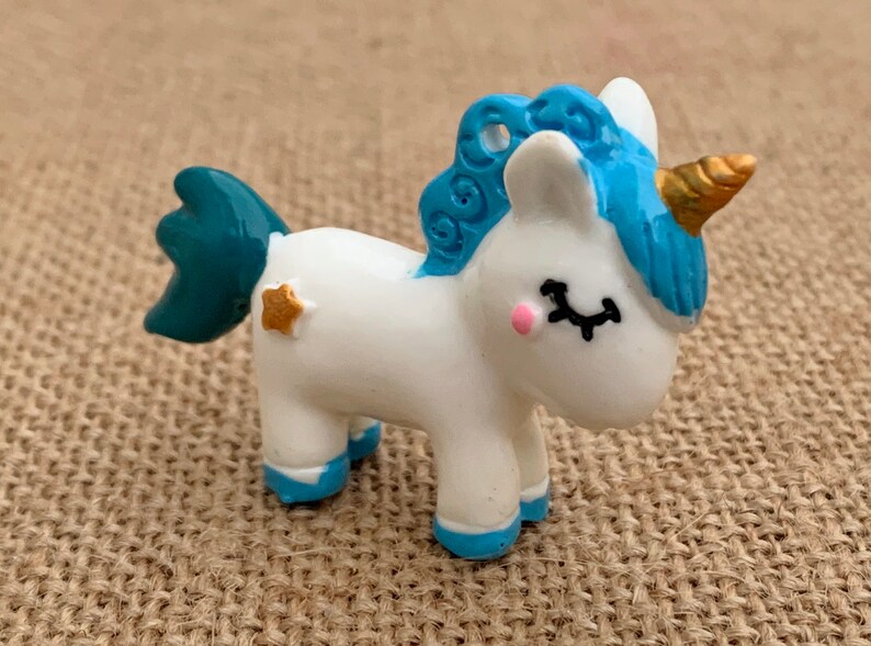 May include: A small white unicorn figurine with a blue mane and tail. The unicorn has a gold horn and a star on its side.